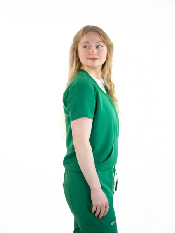 A woman in green scrubs standing up against a white background.