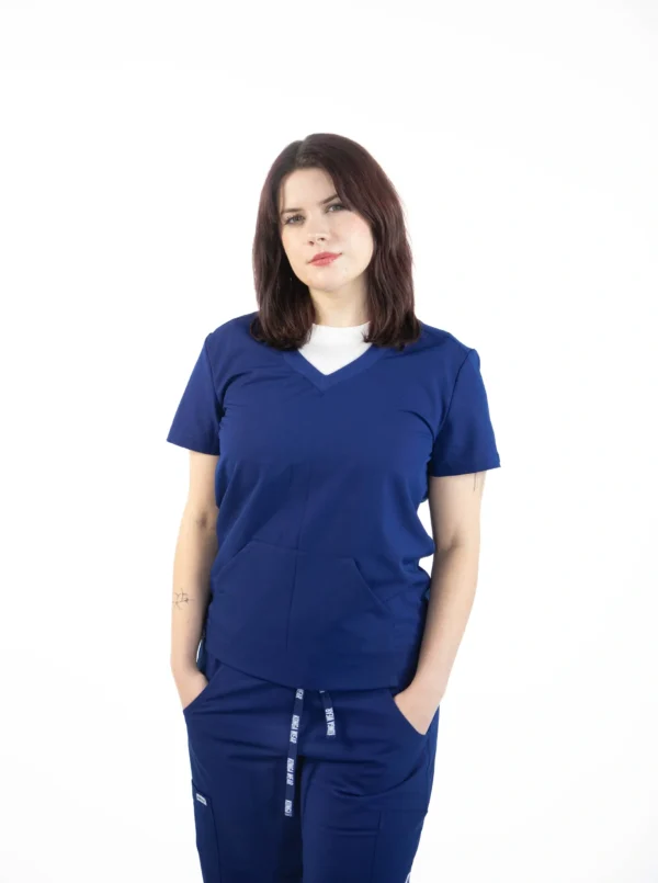 A woman in blue scrubs is standing with her hands in her pockets.