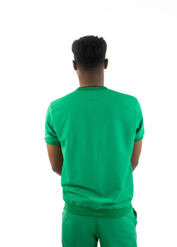 A man in green shirt standing with his hands behind back.