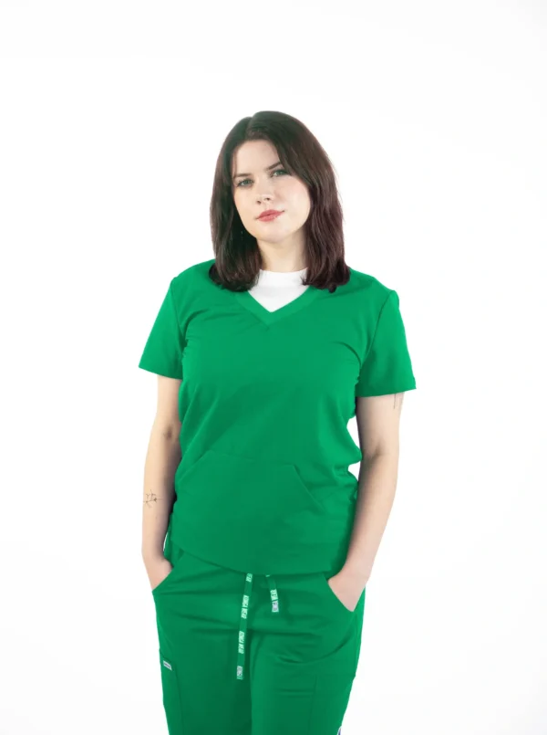 A woman in green scrubs is standing with her hands in pockets.